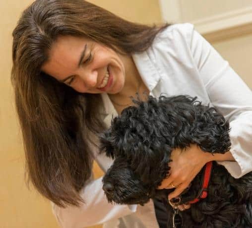 Integrative veterinarian Dr. Julie Buzby wearing her white veterinary coat and examining a happy fluffy dog