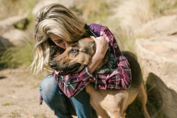 Owner embracing her German Shepherd outside on a trail