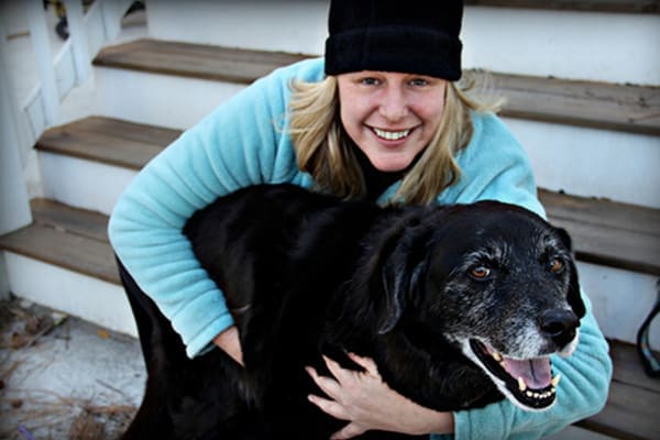 Female owner sitting on steps hugging her elderly black lab, photo