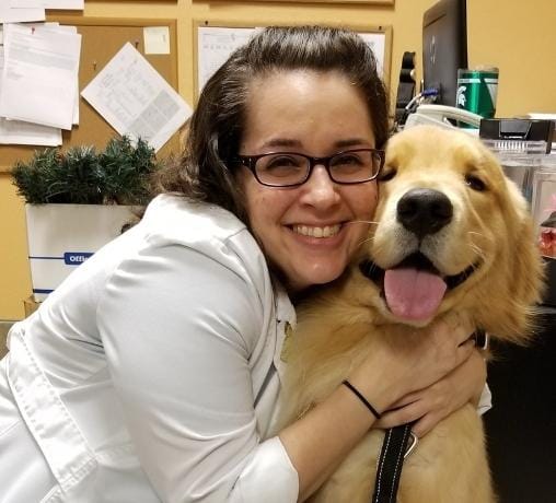 Veterinarian Eric Irsh smiling and hugging a happy Golden Retriever dog