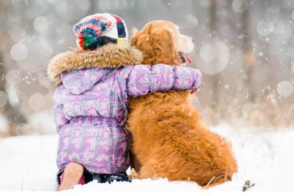 Girl sitting in the snow and hugging her dog 