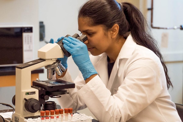 Woman in white lab coat looking through a microscope, photo