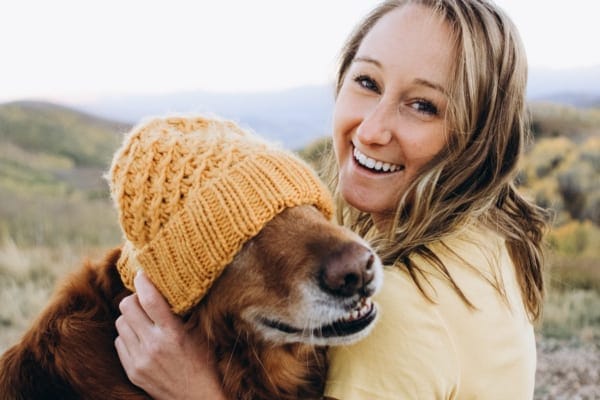 photo senior dog wearing orange knit cap over eyes and girl smiling