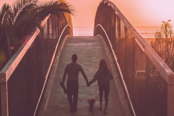 couple walking hand-in-hand over a beach boardwalk with dog, photo