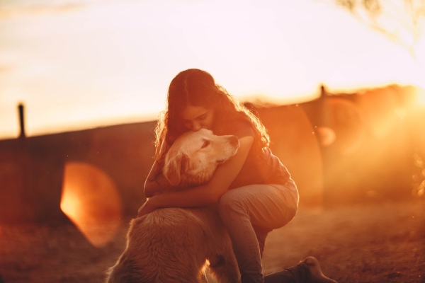 Dog mom hugging her senior dog at sunset as if concerned by her dog's quality of life