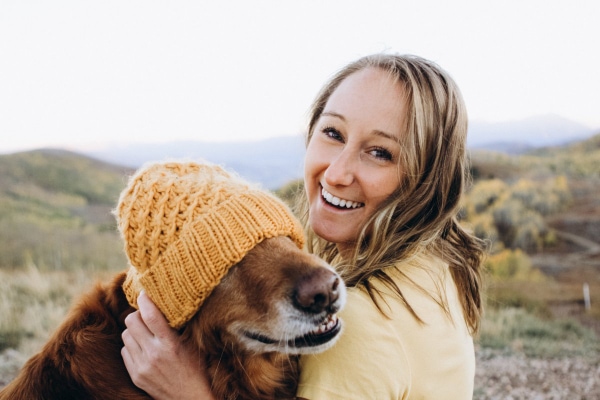 Senior Golden Retriever wearing a knit hat sitting beside a pet parent who may be wondering what age to feed senior dog food