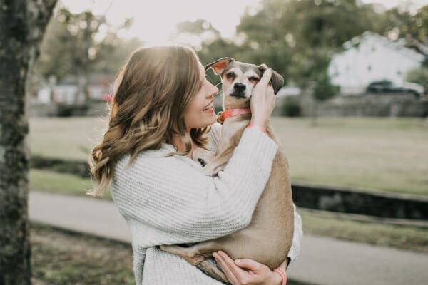 Owner holding a Chihuahua mix outside under a tree, photo